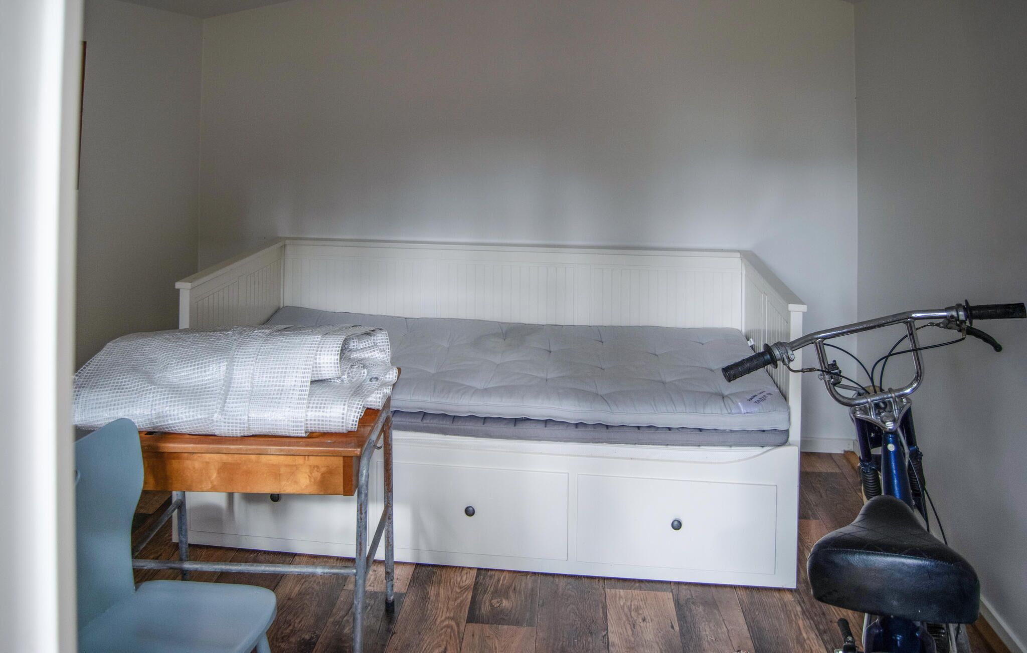 Ein kleines Zimmer mit einem Einzelbett, einem Holztisch und Stuhl, einem Fahrrad und einer Heizung.