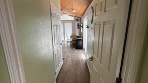 A hallway with wooden ceiling, white doors, and a view into a dining area.