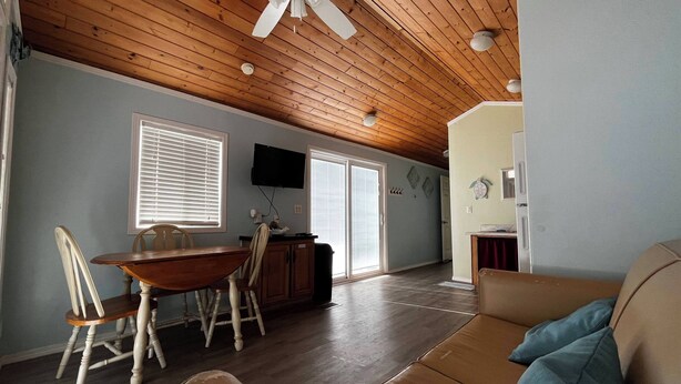 A spacious living area with a wooden ceiling, a dining table with chairs, a sofa, and a television mounted on the wall.