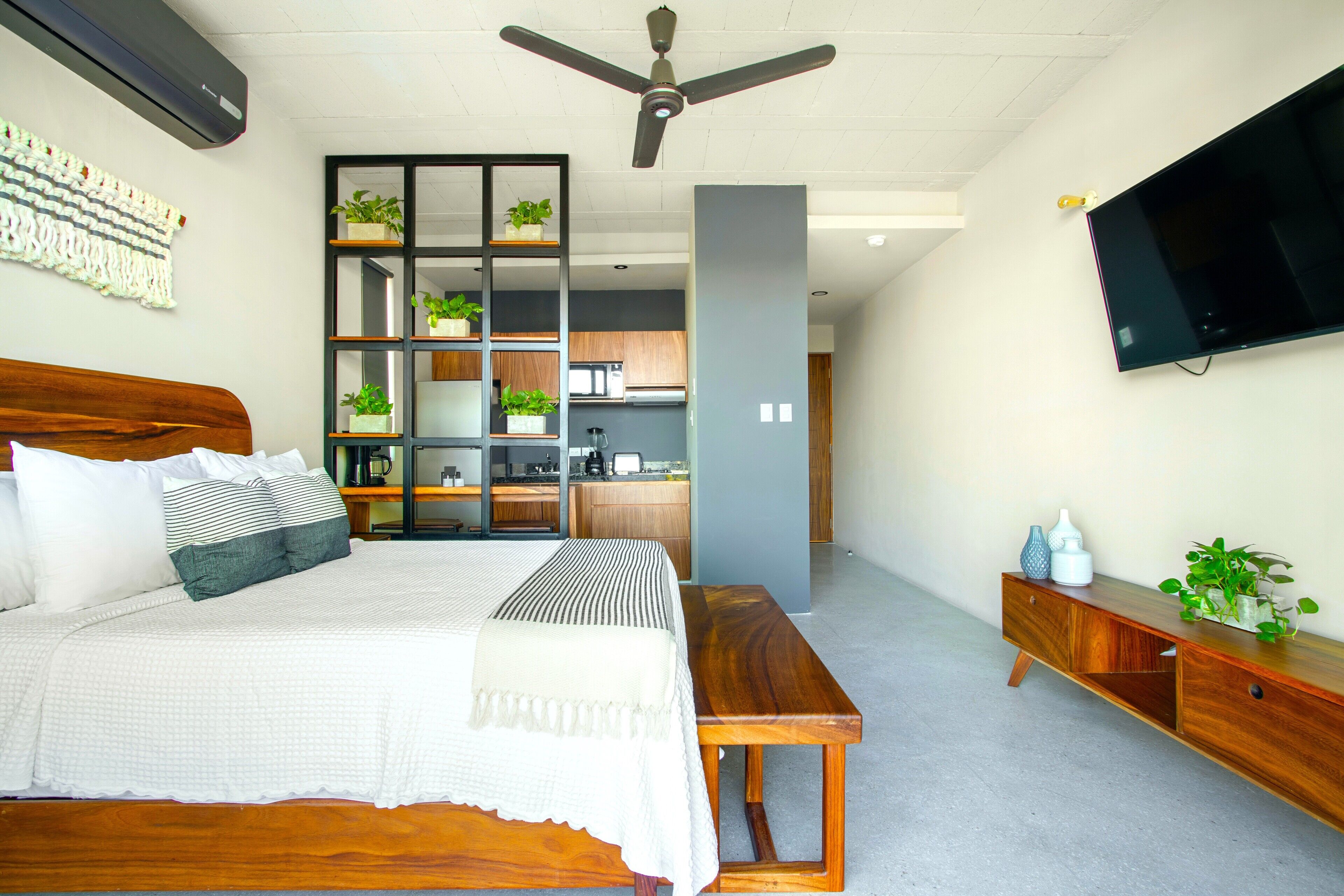 A bedroom with a bed, bedside table, and a built-in kitchen area with cabinets and a countertop.