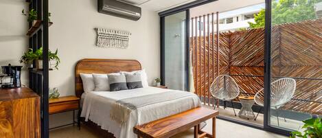 A modern bedroom with a large bed, wooden bench, and a view of a wooden fence through a sliding glass door.