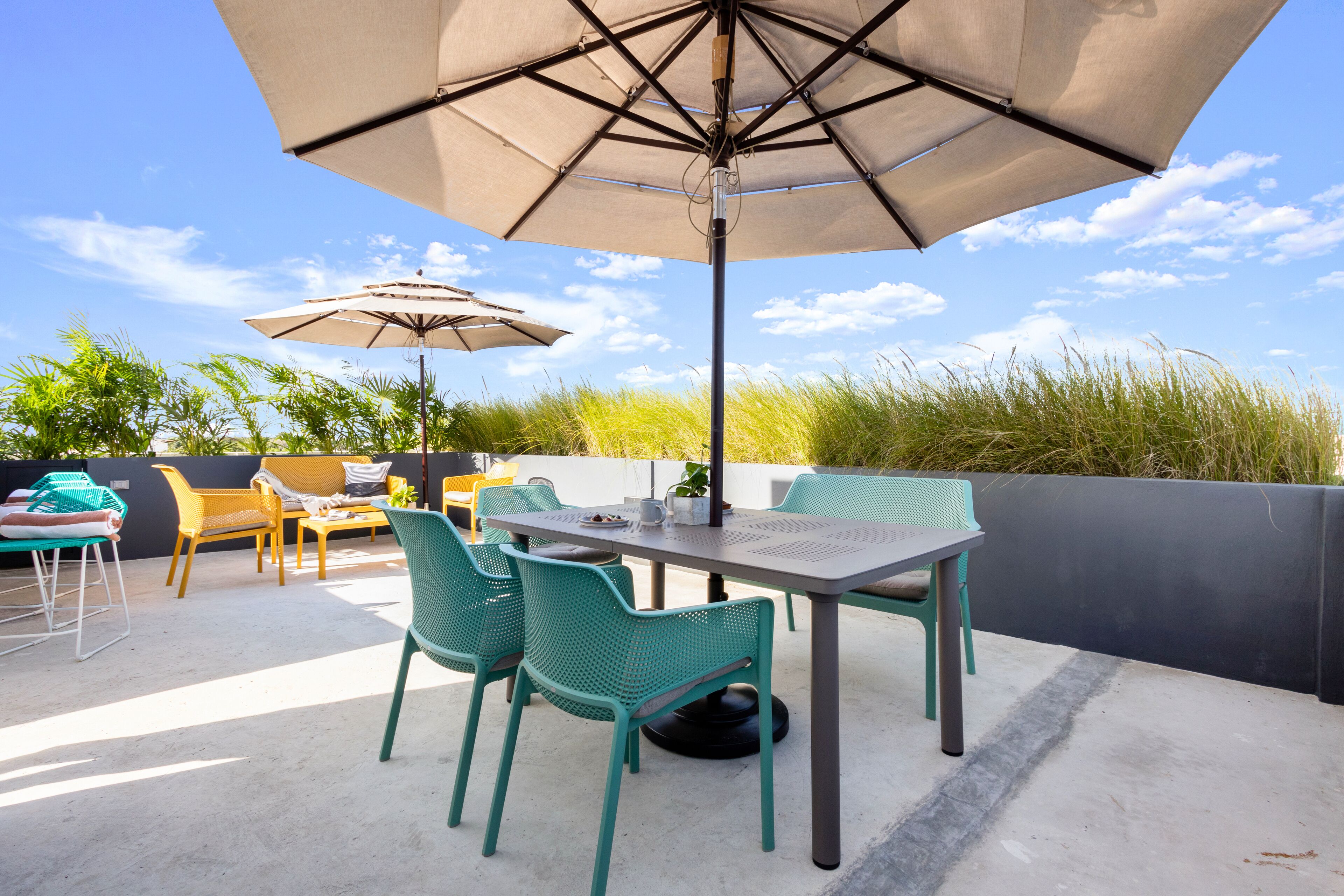 An outdoor patio with a table and chairs, two umbrellas, and a view of the sky and vegetation.