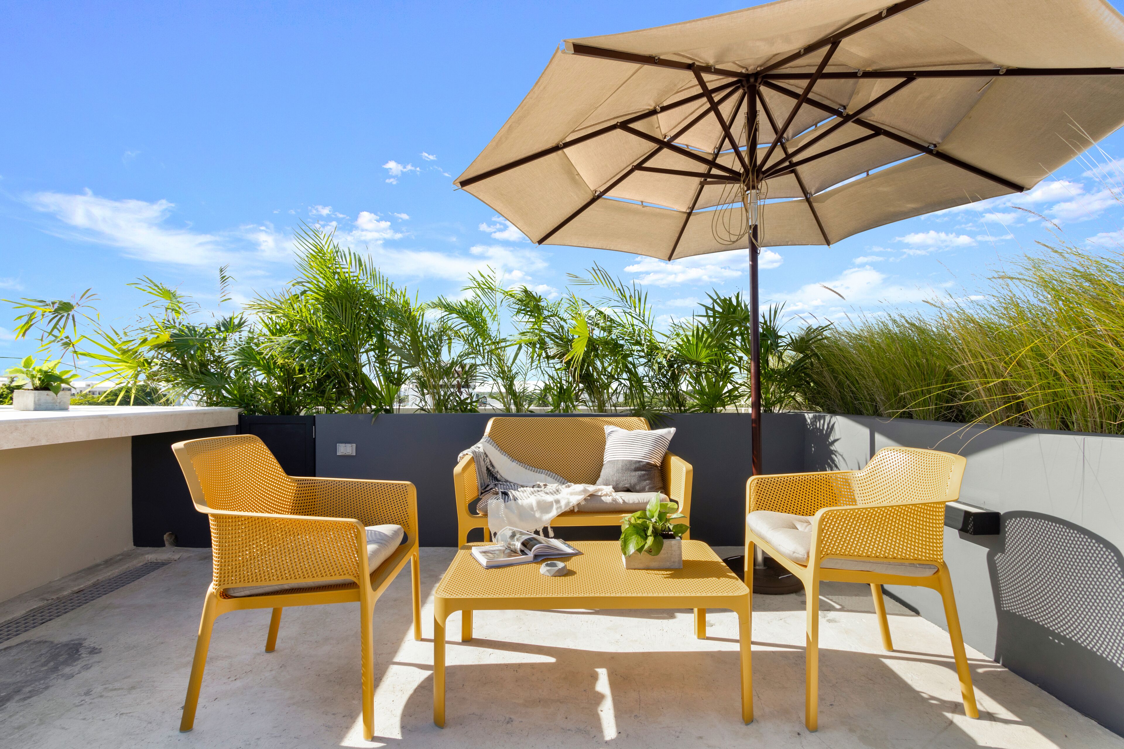 Un espace extérieur aménagé avec des chaises en osier, une table et un grand parasol.