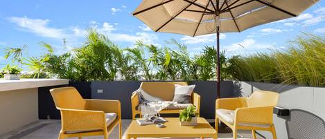 Un espace extérieur aménagé avec des chaises en osier, une table et un grand parasol.