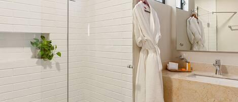 Une salle de bain moderne avec une douche à parois de verre, un mur recouvert de carreaux blancs, un comptoir en marbre et un porte-peignoir suspendu.