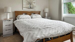 A bedroom with a wooden bed, two bedside tables with lamps, a nightstand, and a window with curtains. - 3 bedroom accommodation in Newton Stewart (Newton Stewart)
