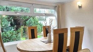 A round wooden dining table with four chairs, a vase with branches, and a view of greenery outside. - 3 bedroom accommodation in Newton Stewart (Newton Stewart)