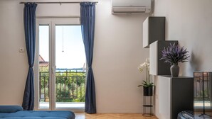 A modern room with a large sliding glass door leading to a balcony, a bed, a small table with a plant, and a mounted air conditioner.