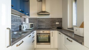 A modern kitchen with white cabinets, a stainless steel oven, a microwave, and a coffee maker.