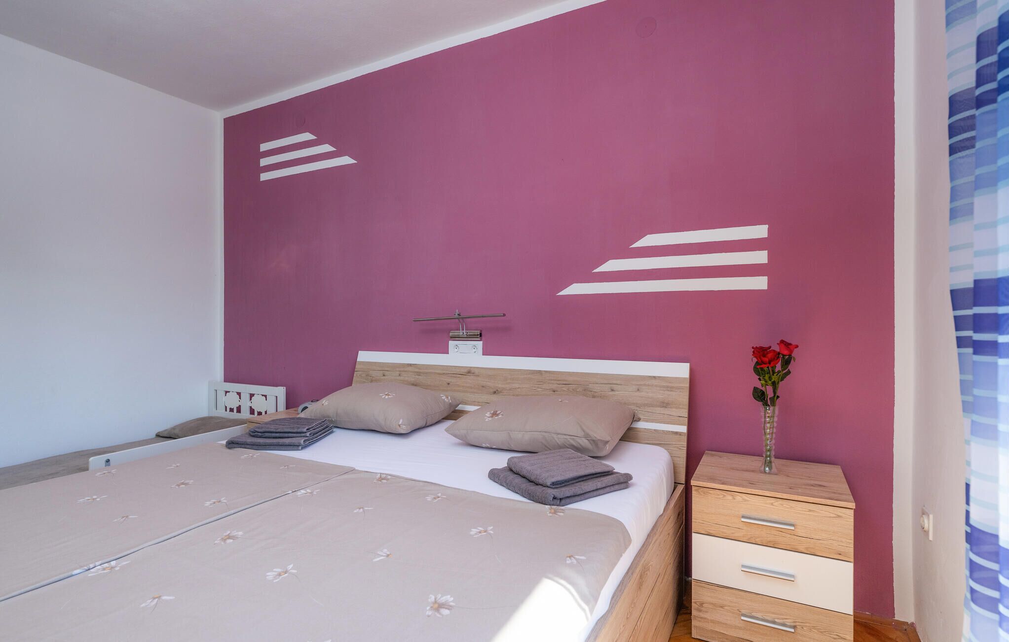 Una camera da letto con un letto, cuscini, un comodino con un vaso di fiori e una parete decorata con arte astratta.