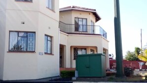 Un immeuble de deux étages avec une façade beige, un balcon à l’étage supérieur et un portail vert en premier plan.