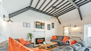 Un soggiorno moderno con camino, divani grigi, cuscini arancioni e un soffitto alto con travi a vista.