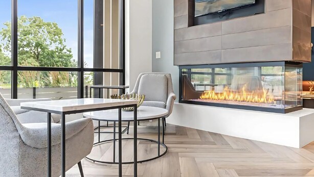 Een moderne woonkamer met een grote televisie, een open haard en een eethoek met een tafel en stoelen.