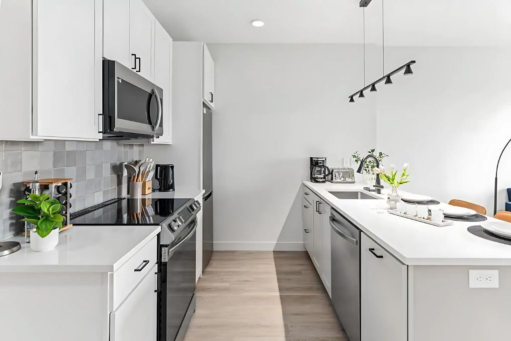 A modern kitchen with white cabinetry, a black microwave, and a stainless steel stove.