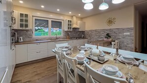 A modern kitchen with white cabinets, a dining table set for six, and a view of a garden through the windows. - Awesome home in Krapinske Toplice (Krapinske Toplice)