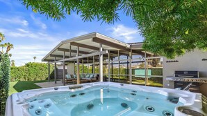 A hot tub with a patio area, a barbecue grill, and a covered seating area with cushions. - Mid Century Modern home -newly renovated with swim jet pool, spa on golf course! (Palm Desert)