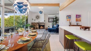 A modern kitchen with a dining area, featuring a wooden ceiling, large windows, and a stone fireplace. - Mid Century Modern home -newly renovated with swim jet pool, spa on golf course! (Palm Desert)
