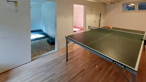A room with a ping pong table, wooden flooring, a door leading to another room, and a small window. - 4 bedroom cozy apartment in Höör (Höör)