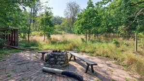 A rustic outdoor area with a stone fire pit, wooden benches, and a paved walkway surrounded by greenery. - 4 bedroom cozy apartment in Höör (Höör)