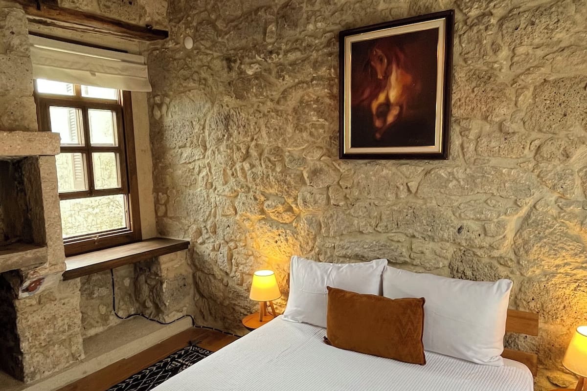 A bedroom with a stone wall, a bed with white bedding, a framed picture, and a hanging light fixture.
