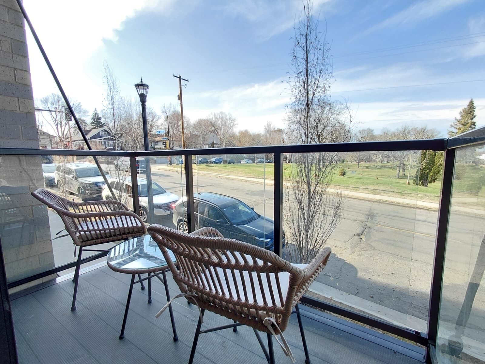 A balcony with wicker chairs, a view of a parking lot, and a street lamp.