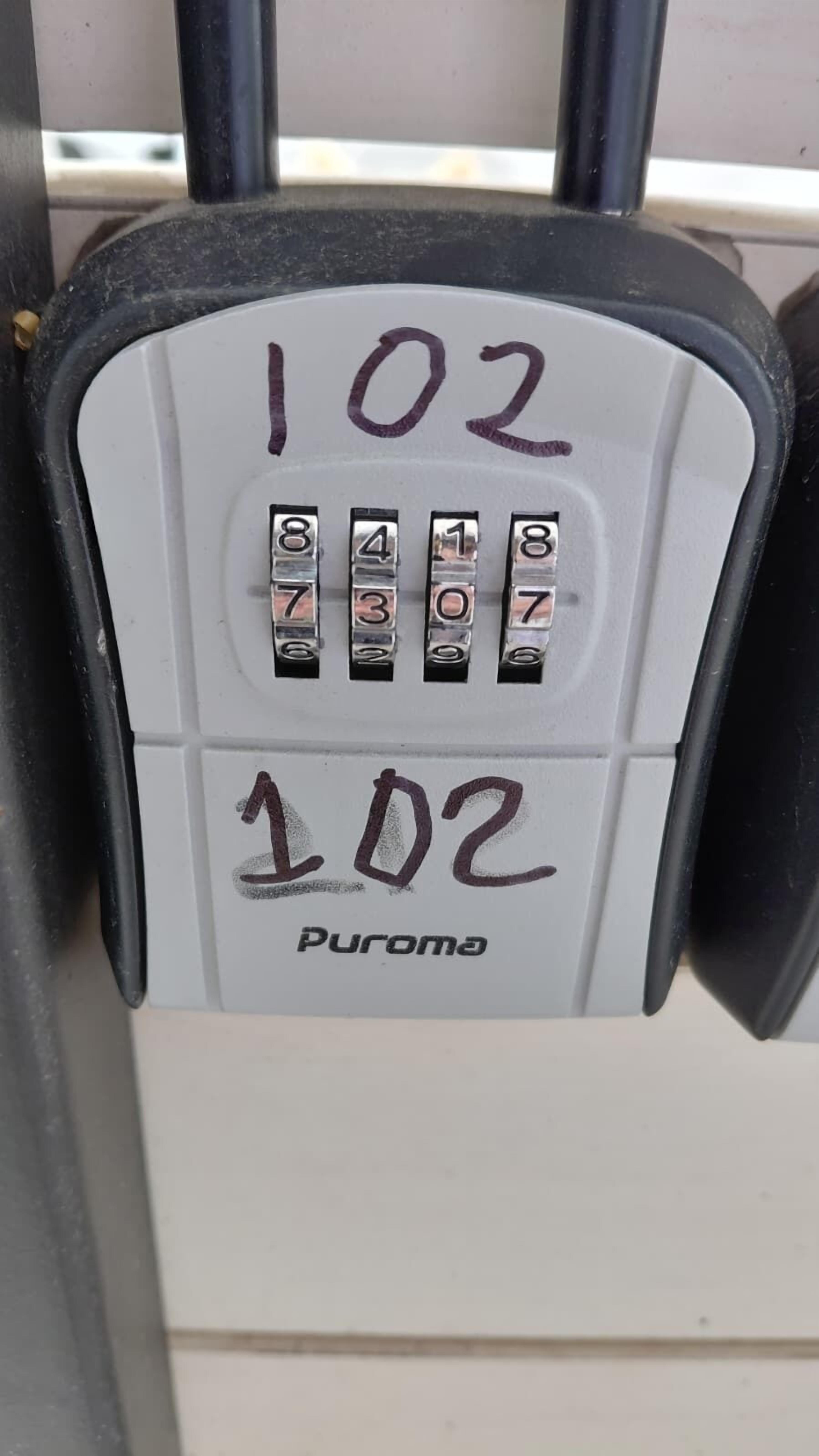 Et tastatur med tal fra 1 til 9 og 0, med teksten '102' og 'Puroma' på en hvid plade.