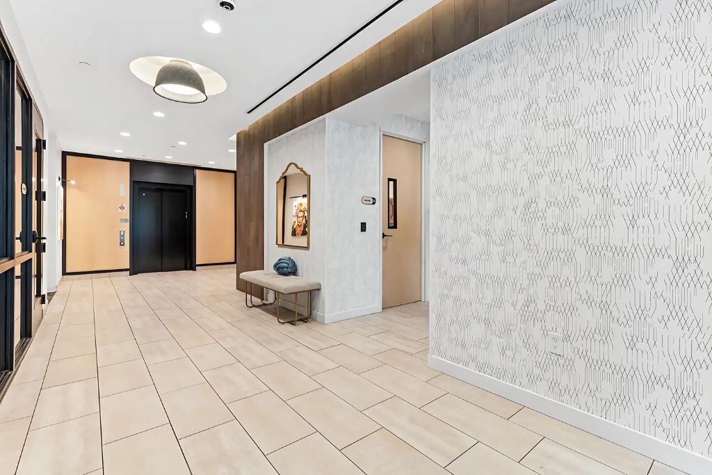 Un hall d’hôtel moderne avec un sol carrelé, un banc, un miroir fixé au mur et un mur décoré de motifs.