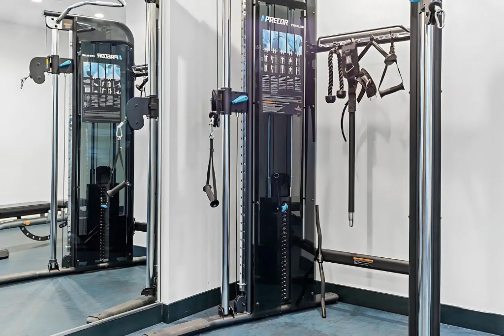 Een fitnessruimte met diverse trainingsapparaten en een spiegelwand.
