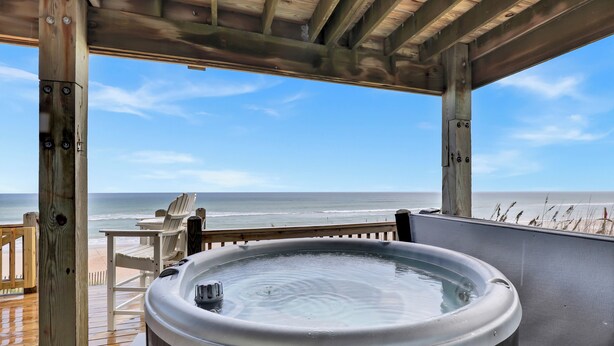A wooden deck with a hot tub, a table, and chairs overlooking the ocean. - Beachfront, HotTub, Elevator, Hammocks, Pet & Familly Friendly (Surf City)