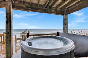 A wooden deck with a hot tub, a table, and chairs overlooking the ocean.