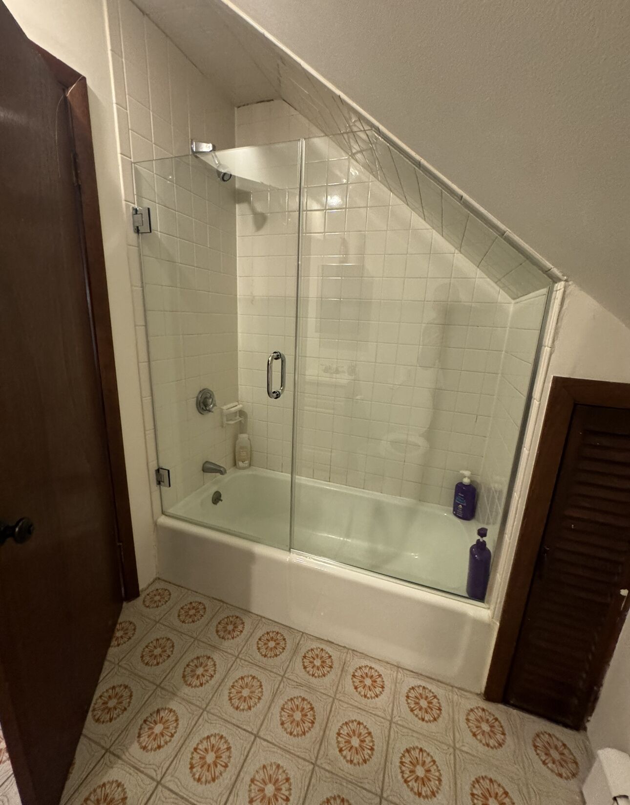 A corner shower with glass doors, a bathtub, and patterned floor tiles.