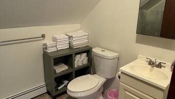 Un baño con inodoro, lavamanos y repisas con toallas.