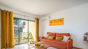 A living room with a sofa, a coffee table, and a sliding glass door leading to an outdoor area with a chair and a table.