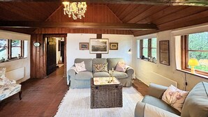 A cozy living room with a wooden ceiling, a chandelier, a grey sofa, and a wicker coffee table. - 2 bedroom beautiful home in Glemmingbro (Glemmingbro)