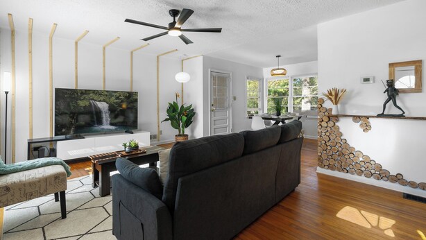 A modern living room with a large flat-screen TV, a dark sofa, a wooden coffee table, and a ceiling fan.