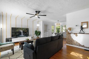 Un salon moderne doté d’un grand téléviseur à écran plat, d’un canapé foncé, d’une table basse en bois et d’un ventilateur de plafond.