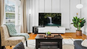 A living room with a large flat-screen TV, a sofa, a coffee table, and a potted plant.