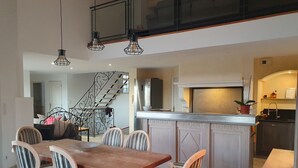 Una cocina amplia con una isla central, un comedor con mesa y sillas de madera, y una escalera que sube a un nivel superior.