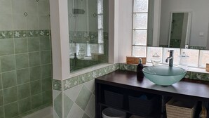 Un baño con cabina de ducha de vidrio, un espejo grande y un lavamanos de vidrio sobre una encimera oscura.