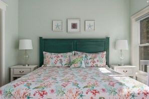 Uma cama com roupa de cama florida, duas mesas de cabeceira com abajures e uma cabeceira verde-água.