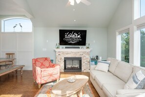 A living room with a fireplace, a television mounted above it, and a large window with two birds perched outside.