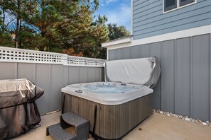 A hot tub with a cover, a step stool, and a patio area with a fence and trees in the background. - Salty Breeze: Oceanside, Elevator,Hot Tub, Community Pool Access! (Corolla)