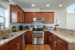 A modern kitchen with wooden cabinets, stainless steel appliances, granite countertops, and a large window.