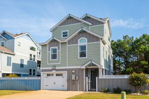 A multi-story residential building with a garage, a covered entryway, and a visible address number. - Salty Breeze: Oceanside, Elevator,Hot Tub, Community Pool Access! (Corolla)
