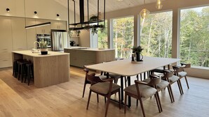 Eine moderne Küche mit einer zentralen Kochinsel, Holzboden und großen Fenstern mit Blick auf Bäume.