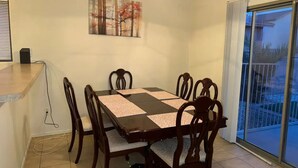 A dining area with a table, chairs, a chandelier, a painting, and a sliding glass door to the outside.