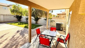 A covered patio area with a table and chairs, a small lawn, and a brick wall.
