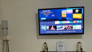 A flat-screen TV mounted on a wall displaying a streaming service interface with various content options.