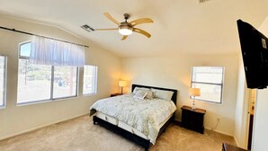 A bedroom with a bed, two bedside tables with lamps, a ceiling fan, and a TV on the wall.