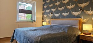 A bedroom with a bed, two bedside lamps, a window with blinds, and a wall with a bird pattern.